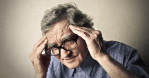 old man wearing glasses holding his head with his hands. 